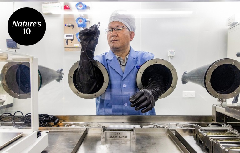 Portrait of Li Chunlai holding a piece of moon rock in a pair pf tweezers inside a glove box